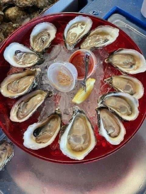 Plate of raw oysters on ice with lemon wedges and cocktail sauce on a red tray