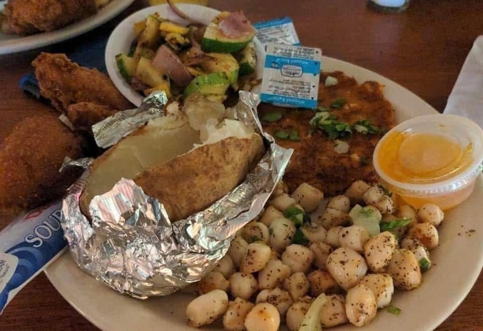 Foil-wrapped baked potato with sides of potatoes, salad, and dipping sauce on a plate in a restaurant