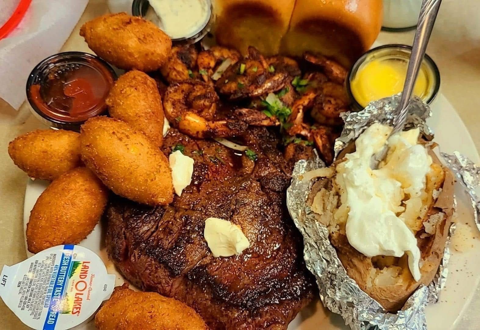 Plated steak dinner with croquettes, baked potato, sauces, and bread rolls