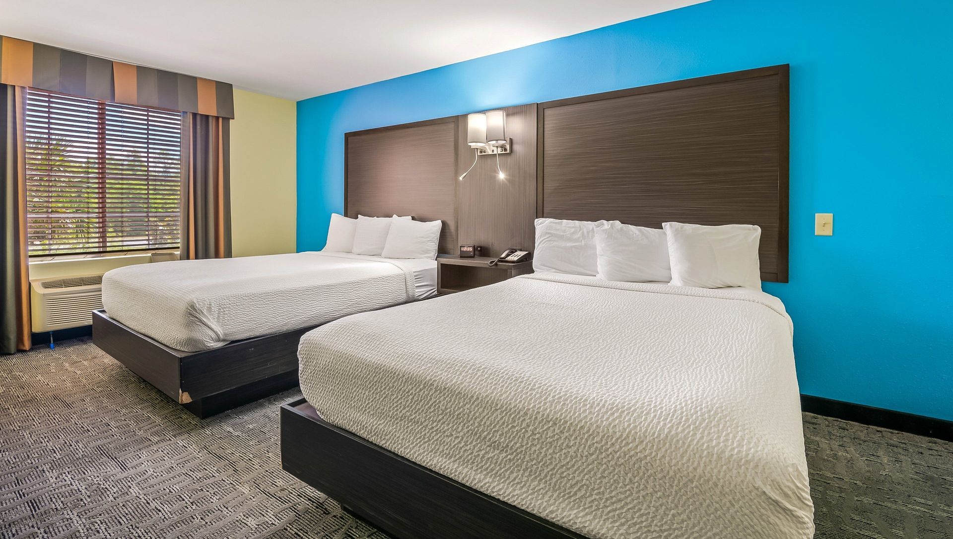 Hotel room with two double beds, teal accent wall, and window with curtains