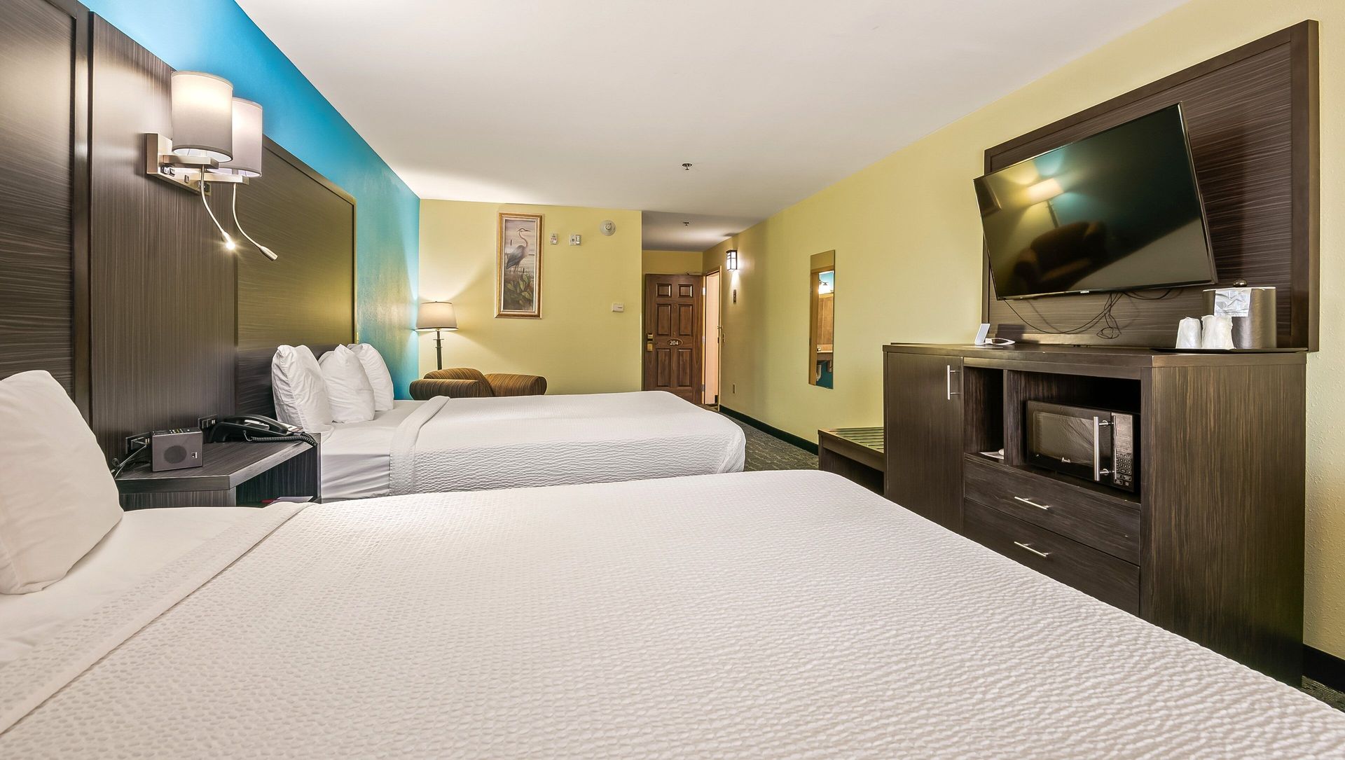 Hotel room with two beds, dark wood furniture, TV, and teal accent wall