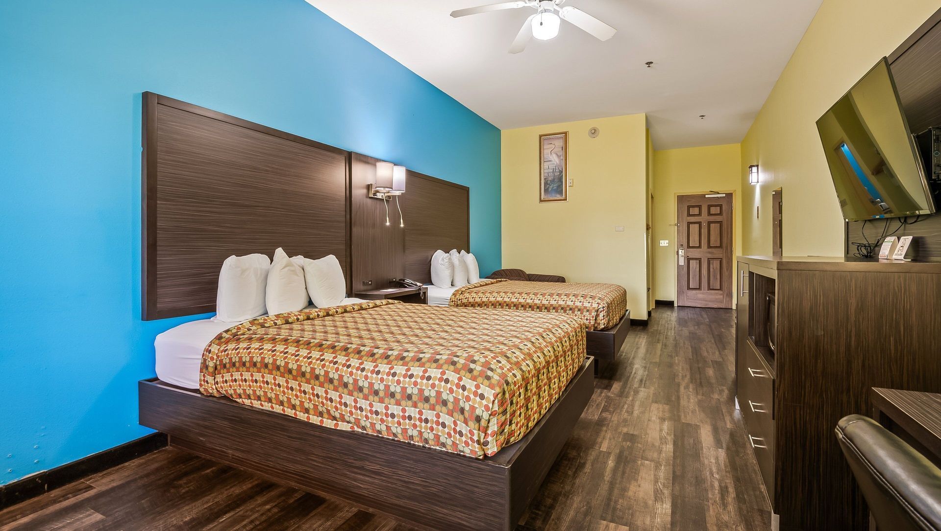 Hotel room with two beds, brown headboards, blue and yellow walls, and wood flooring
