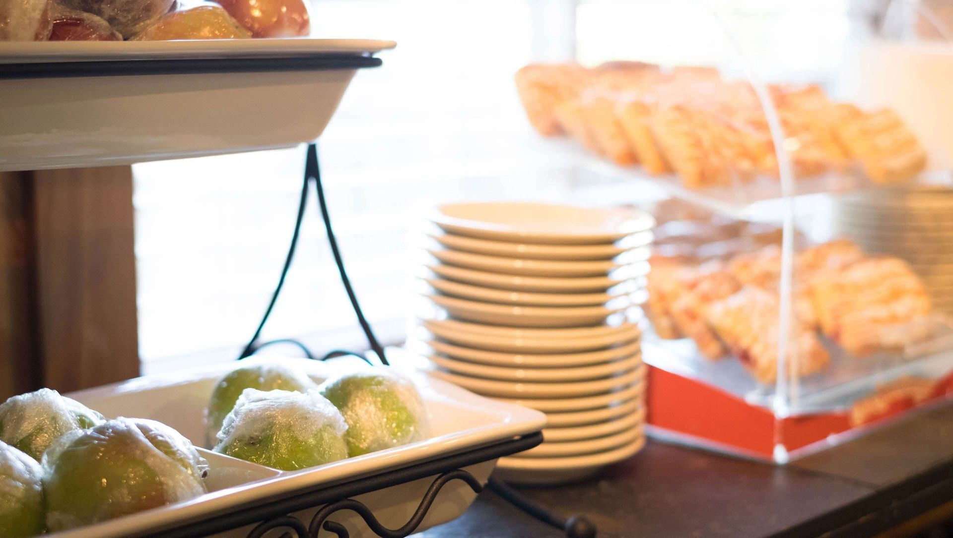 Pastries and rolls displayed on a bakery counter beside stacked plates and covered pastries