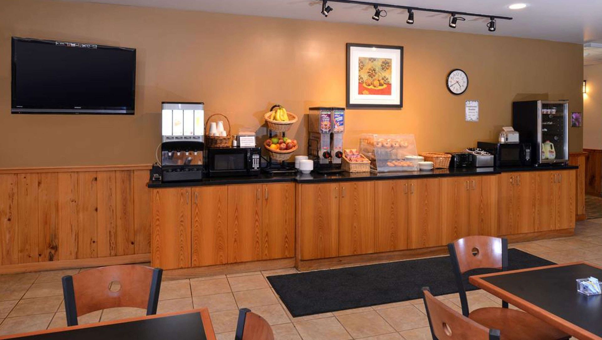 Buffet-style dining area with wooden counter, coffee station, wall TV, and framed art.