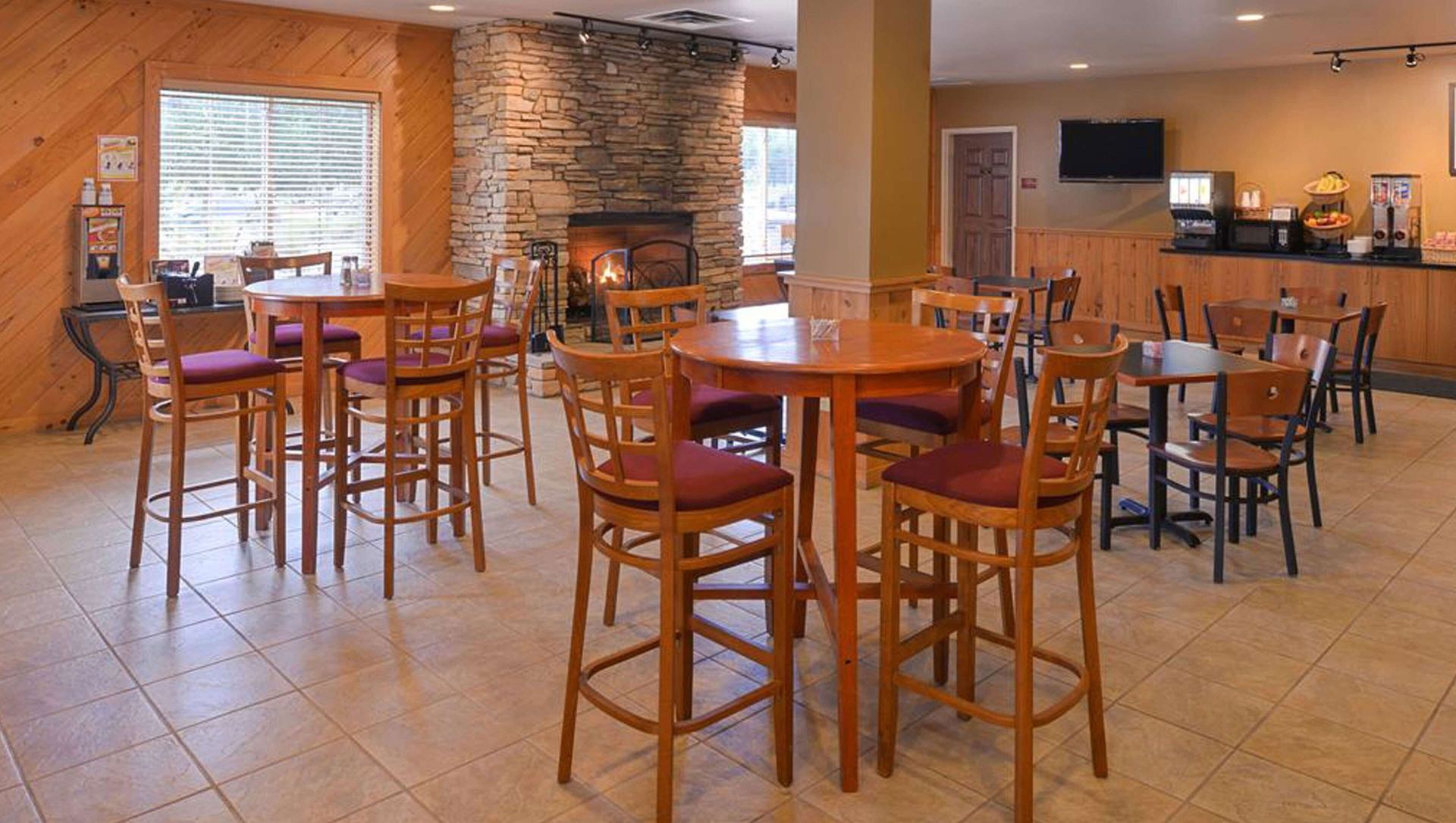 Empty café seating area with wooden tables and chairs, stone accent wall, and tiled floor.