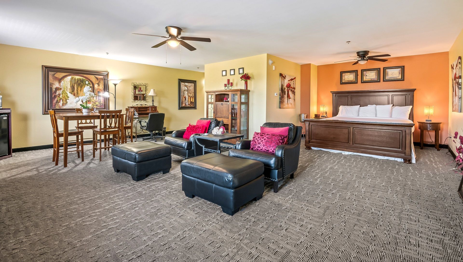 Spacious living room with dark sofas, patterned carpet, ceiling fan, and piano against orange walls.