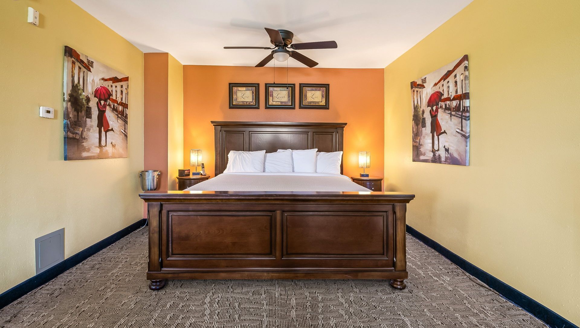 Warm bedroom with wooden bed, orange accent wall, patterned carpet, and ceiling fan