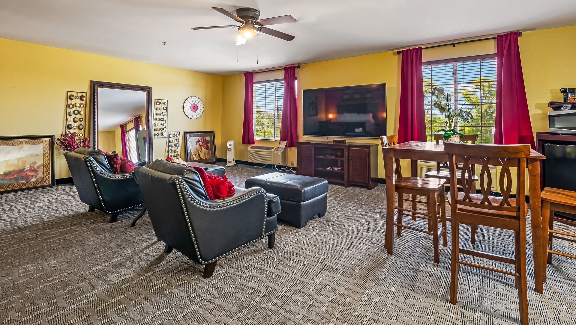 Bright living room with black chairs, large TV, fireplace, dining table, and sunlit windows
