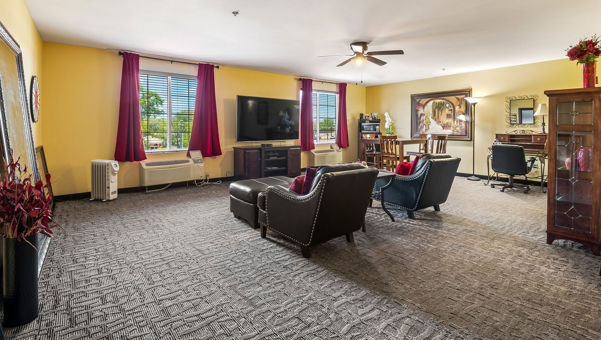 Spacious living room with patterned carpet, two chairs, TV, fireplace, and large windows with red curtains