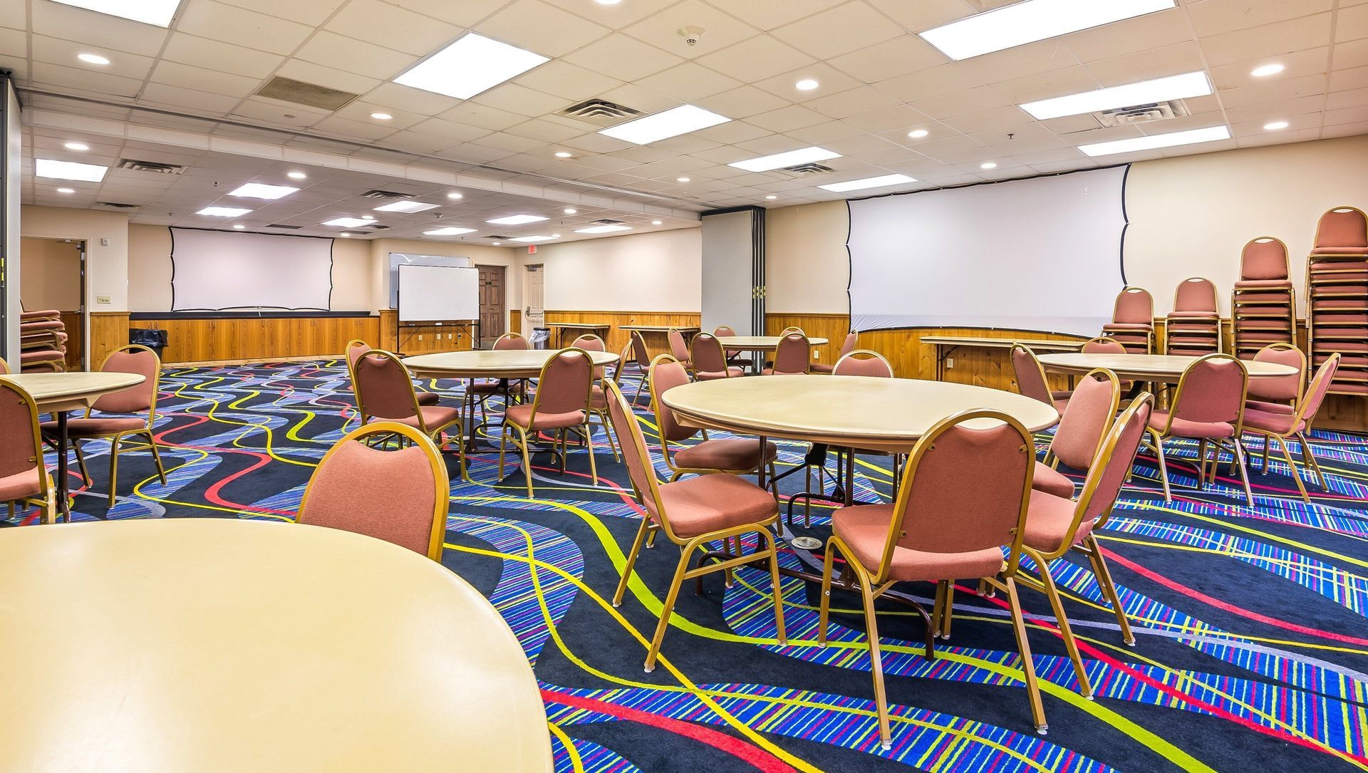 Empty conference room with round tables, orange chairs, and colorful carpet under bright ceiling lights