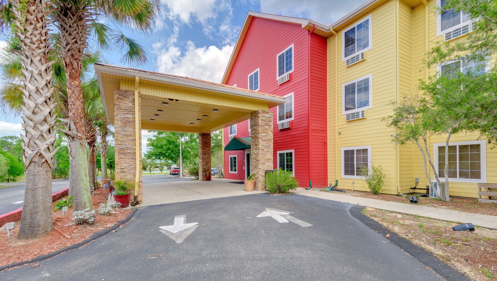 Covered entrance to a colorful apartment building with palm trees and parking arrows on the pavement