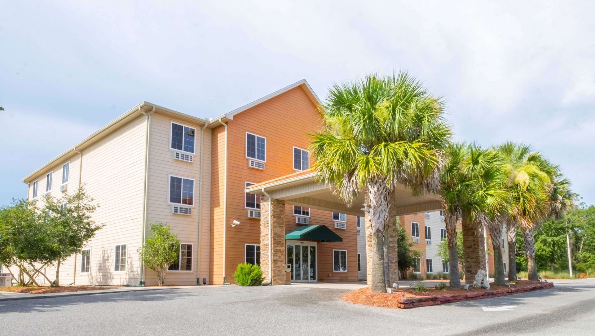 Three-story apartment building with palm trees and a covered entrance on a sunny day