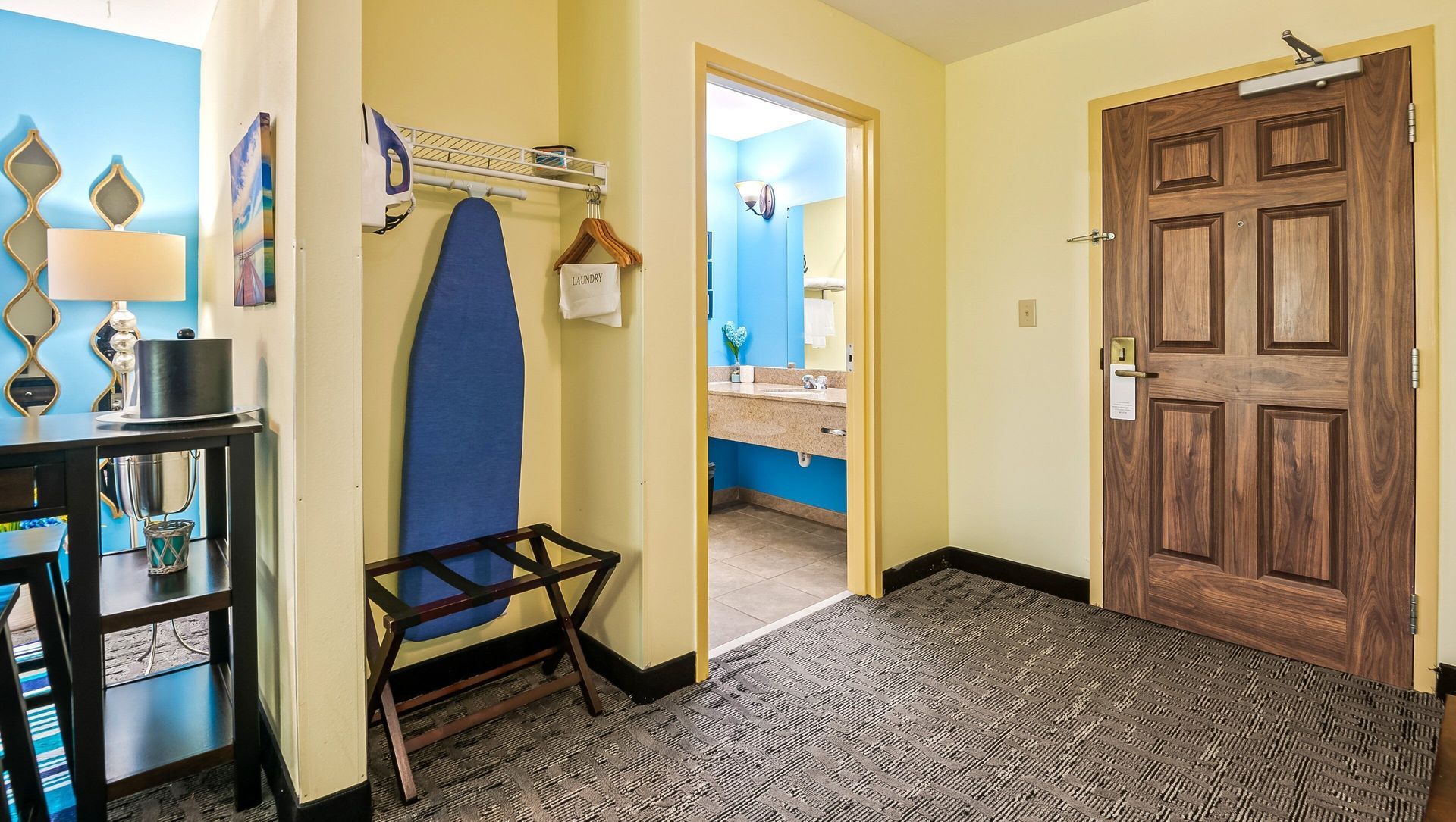 Entryway with wooden door, bench, wall mirror, and blue surfboard decor on yellow walls