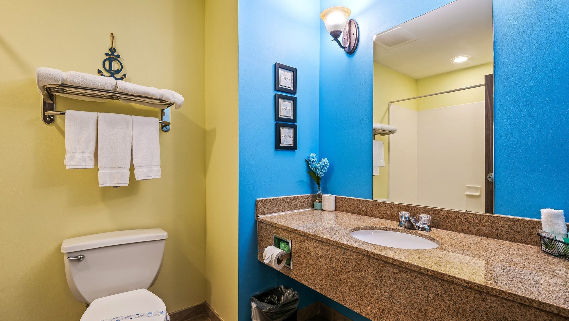 Small bathroom with a toilet, granite vanity, blue and yellow walls, and towels on a rack.