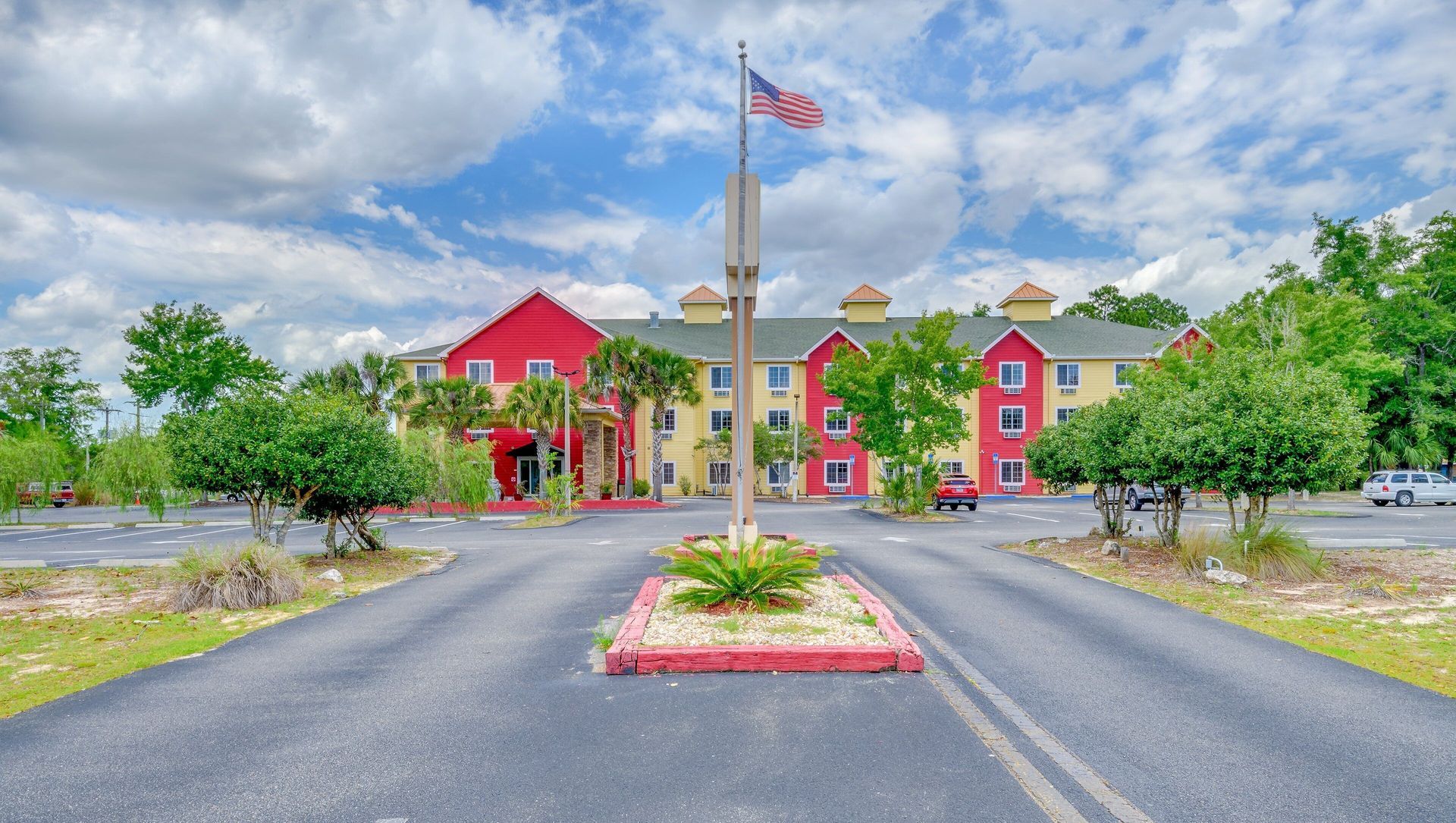Colorful resort entrance with a central driveway, flagpole, and landscaped roundabout under a cloudy sky