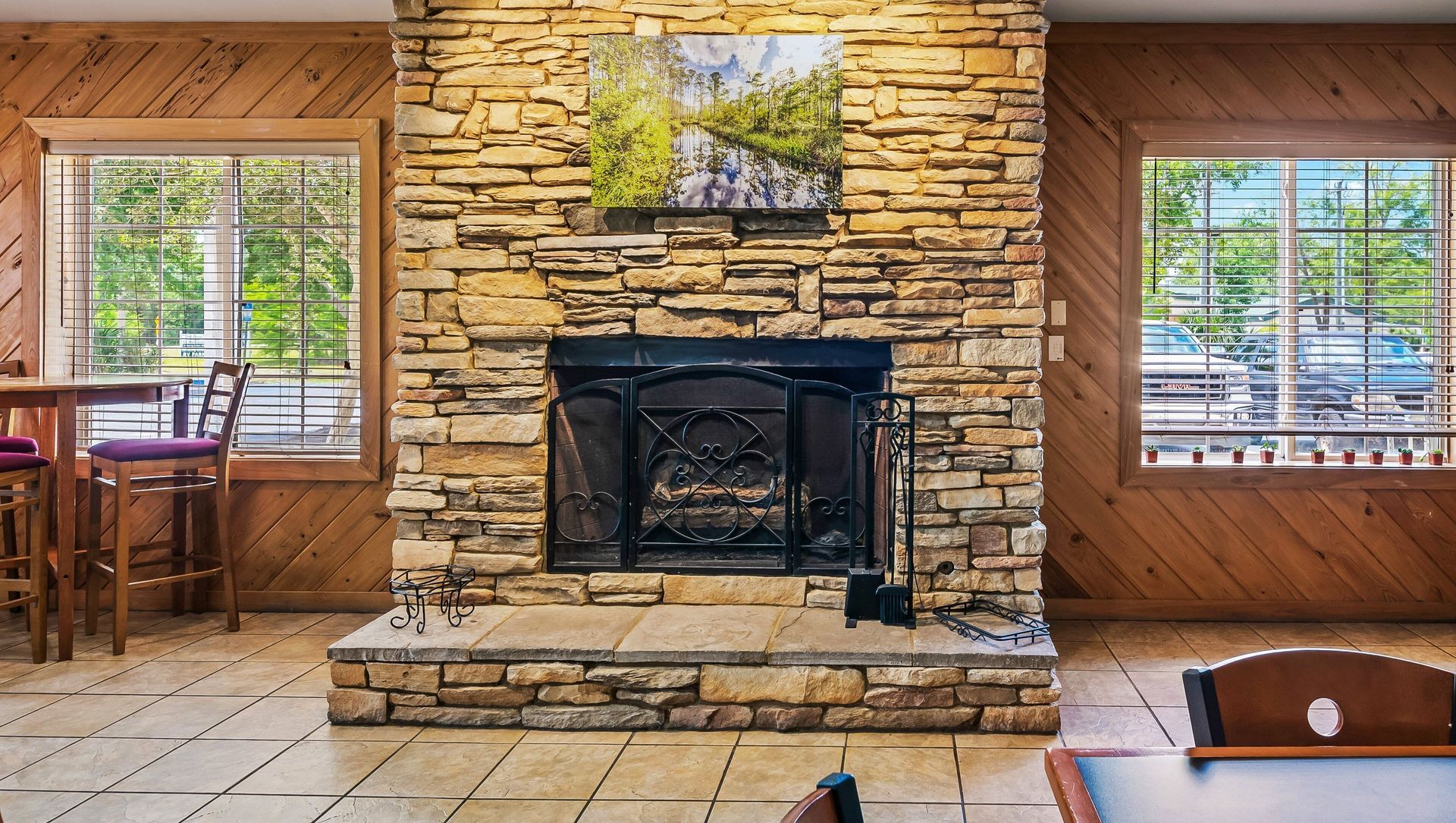 Stone fireplace in a cozy room with wood-paneled walls and windows on either side