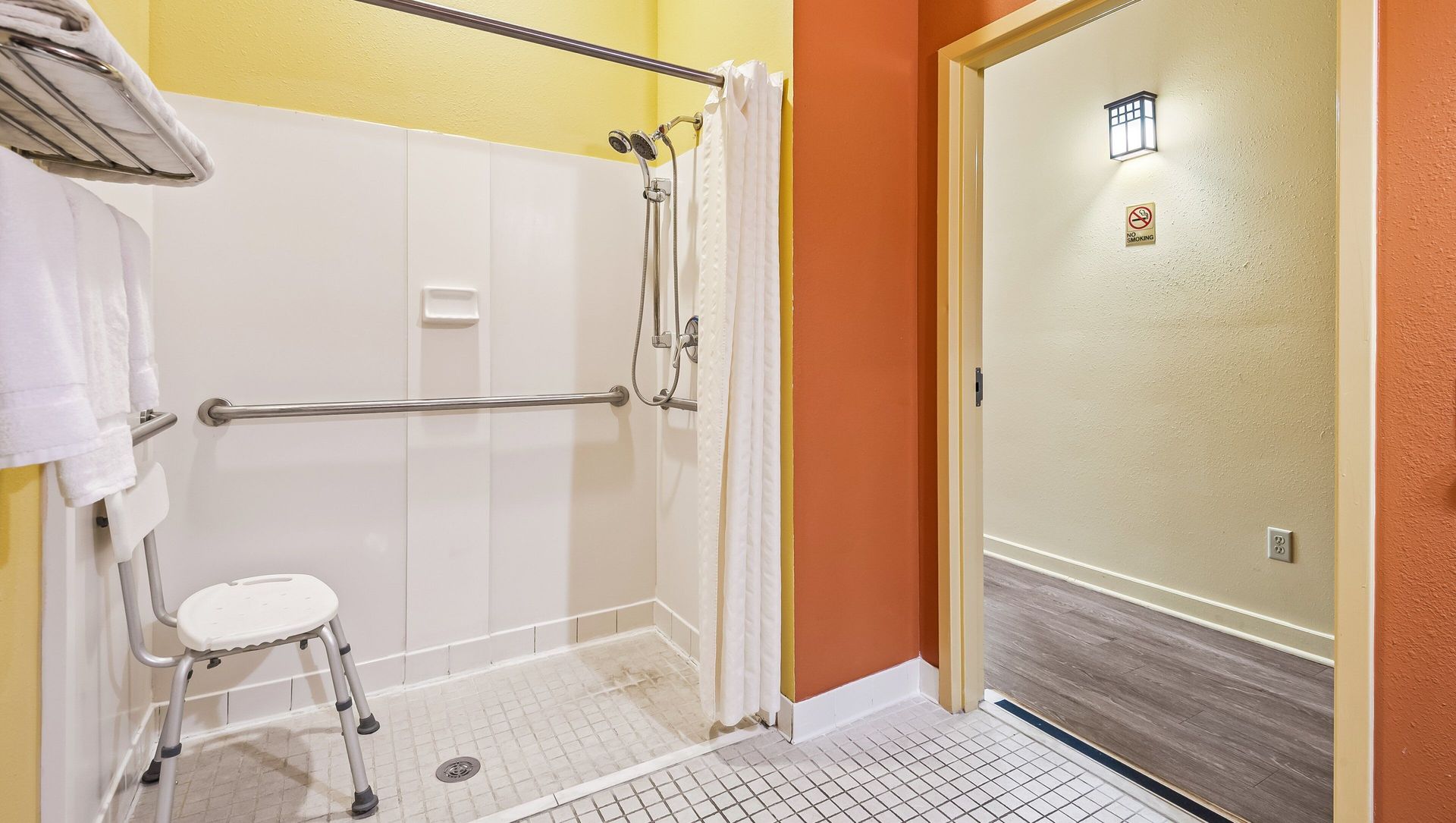 Accessible bathroom with a roll-in shower, grab bars, shower chair, and orange accent wall