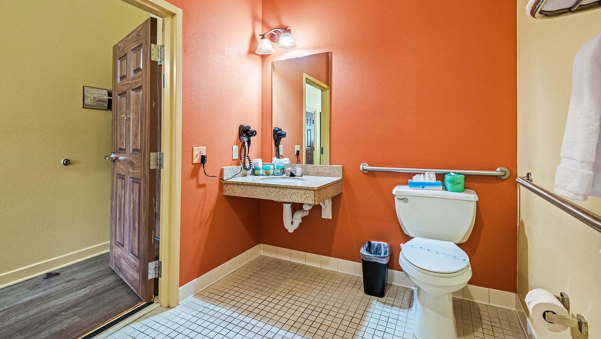 Small bathroom with orange wall, white toilet, wall sink, mirror, and open wooden door to hallway