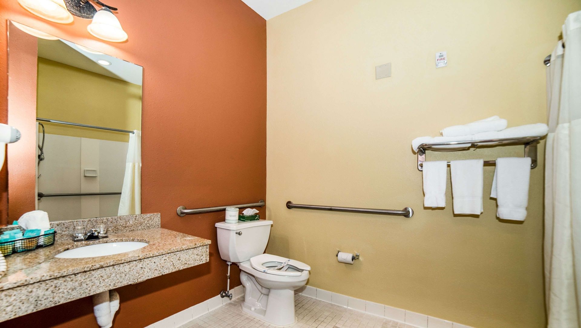 Bathroom with granite vanity, toilet, bidet, beige walls, wall shelves, and tiled floor.