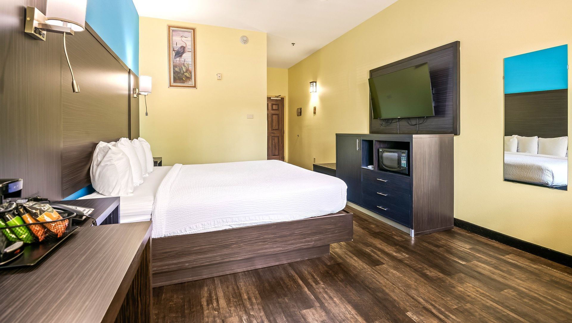 Compact hotel room with a bed, TV, dresser, and dark wood flooring.