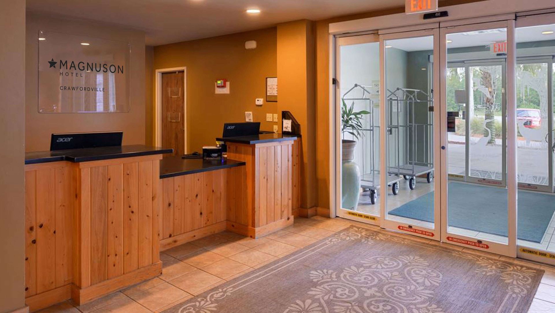 Empty hotel lobby with wooden reception desk, glass doors, and patterned rug