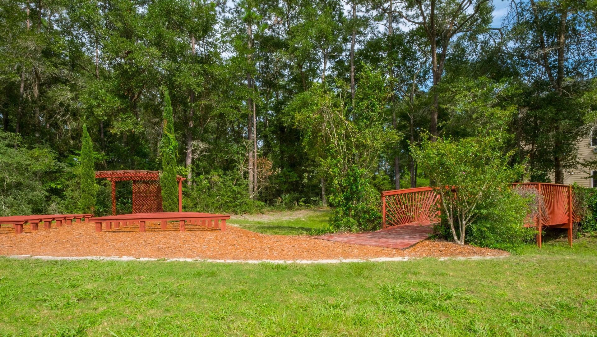 Outdoor exercise area with orange workout equipment on a gravel path, surrounded by trees and grass