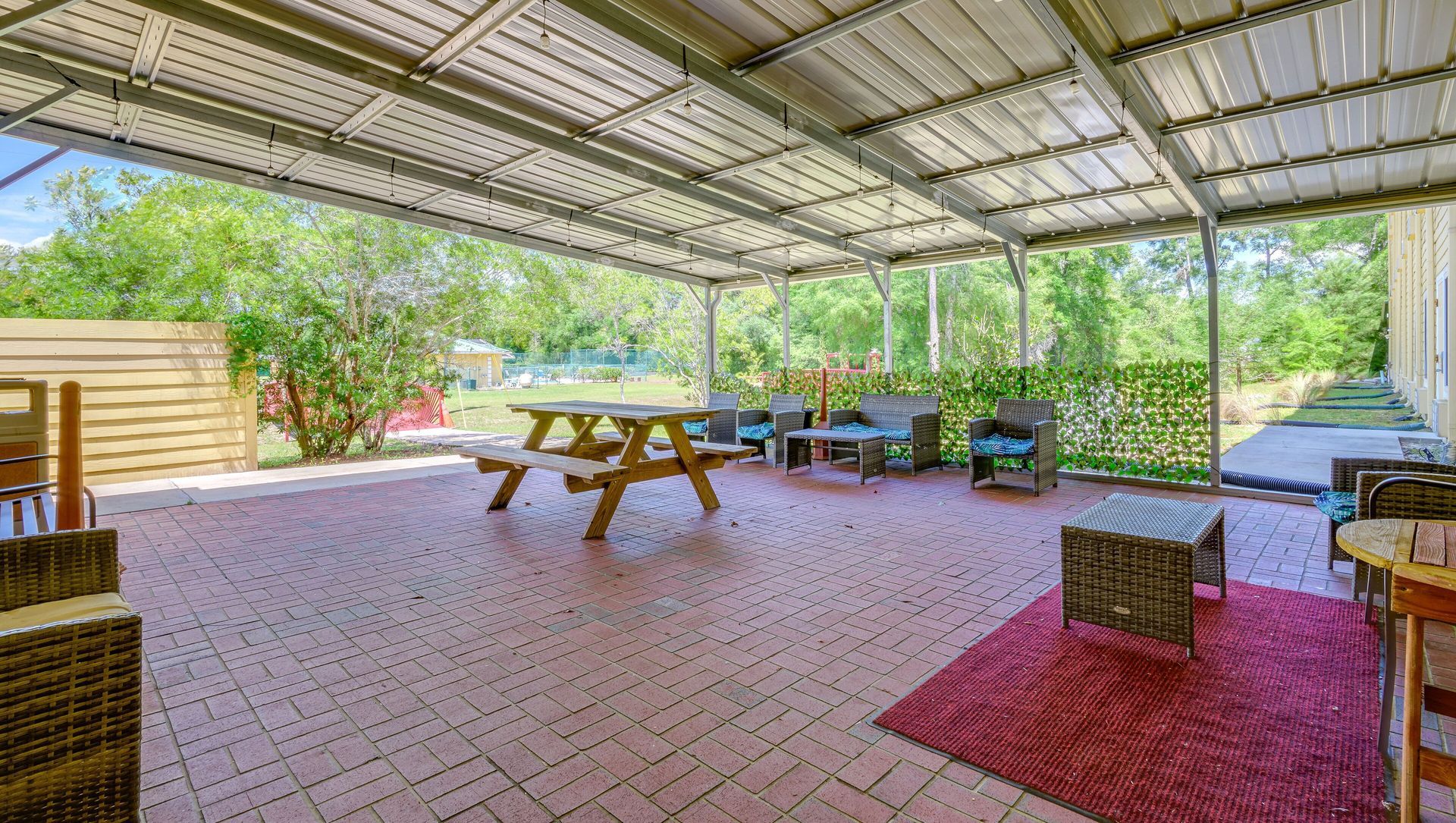 Covered patio with picnic tables, chairs, and greenery in an open-air outdoor dining area.