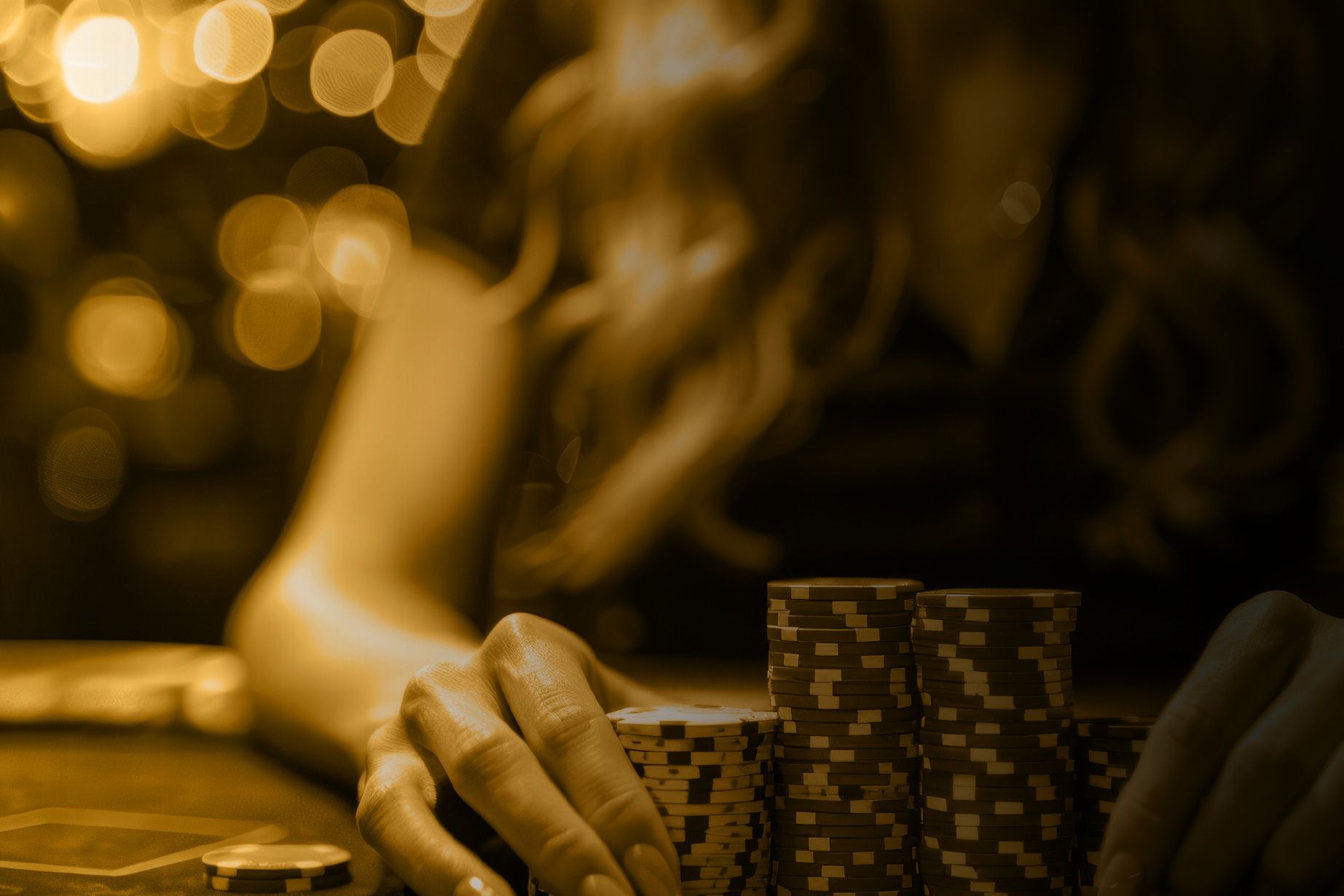A person is sitting at a table holding a pile of poker chips.