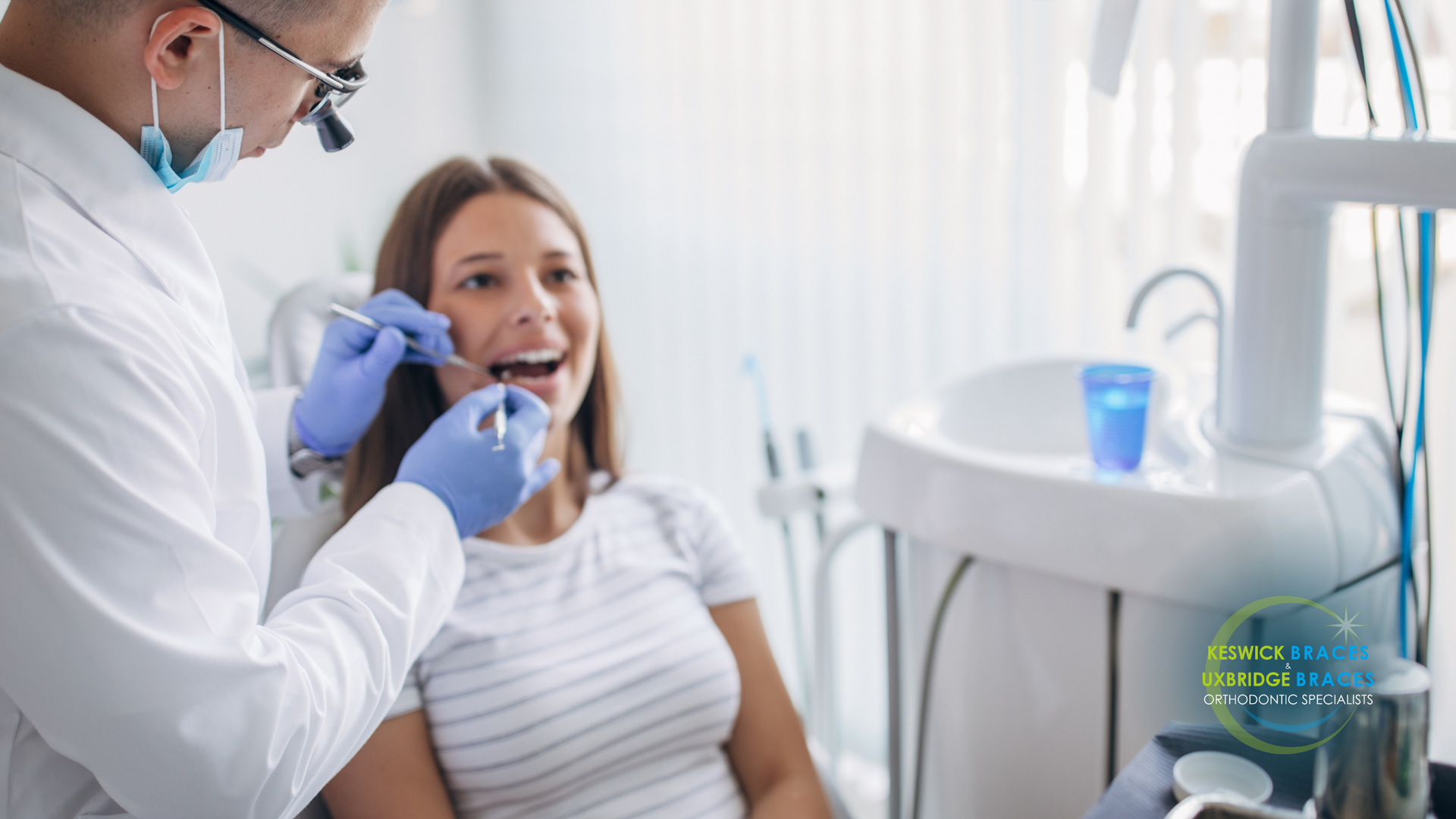 A woman is sitting in a dental chair while a dentist examines her teeth.