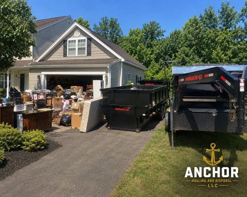 Moving truck and cluttered garage sale items outside a suburban house on a sunny day
