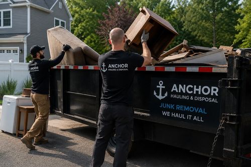 Workers loading furniture into a black Anchor junk removal dumpster outdoors