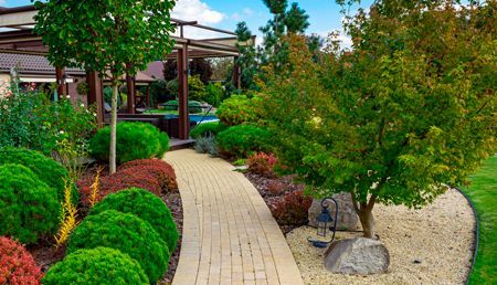 A brick walkway in a garden surrounded by trees and bushes.