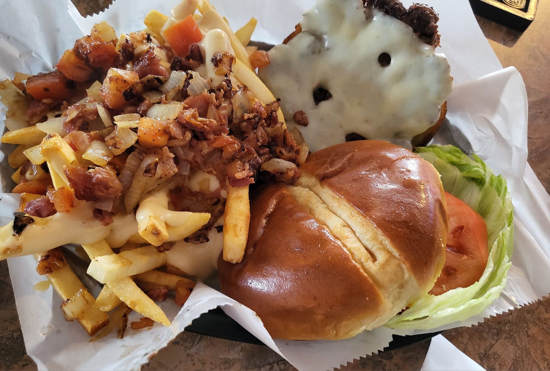 Burger on pretzel bun with fries topped with meat and onions.