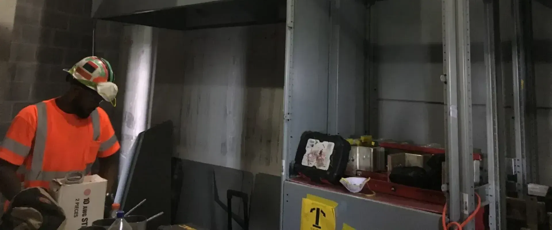 A man in an orange shirt is standing in a room next to a machine.