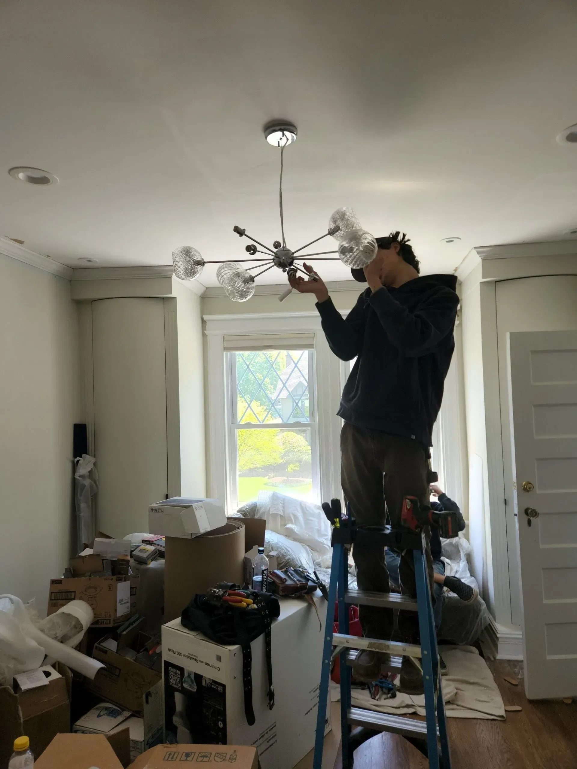 A man on a ladder installing a chandelier in a living room