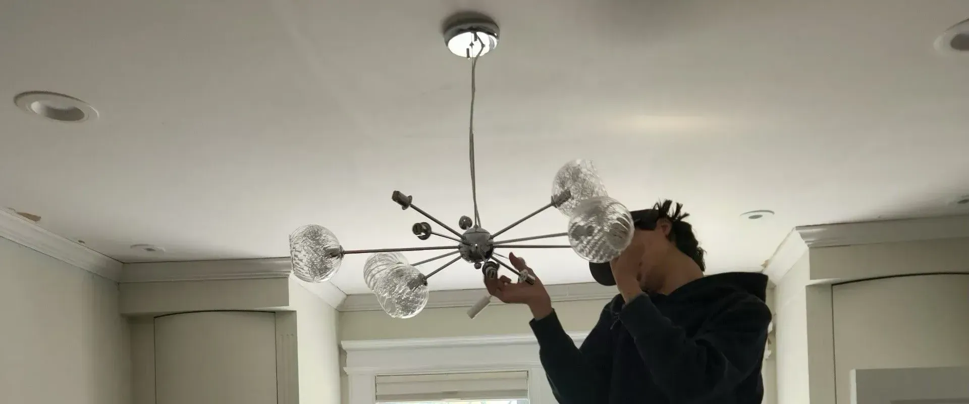 A man on a ladder installing a chandelier in a living room