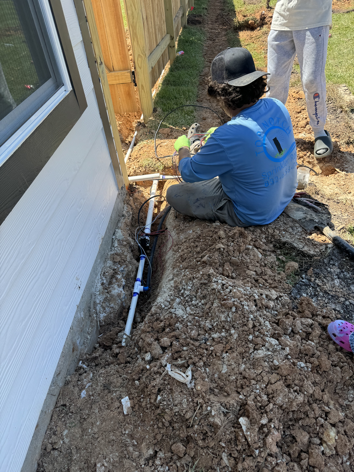 A man in a striped shirt is squatting down to fix a fence.