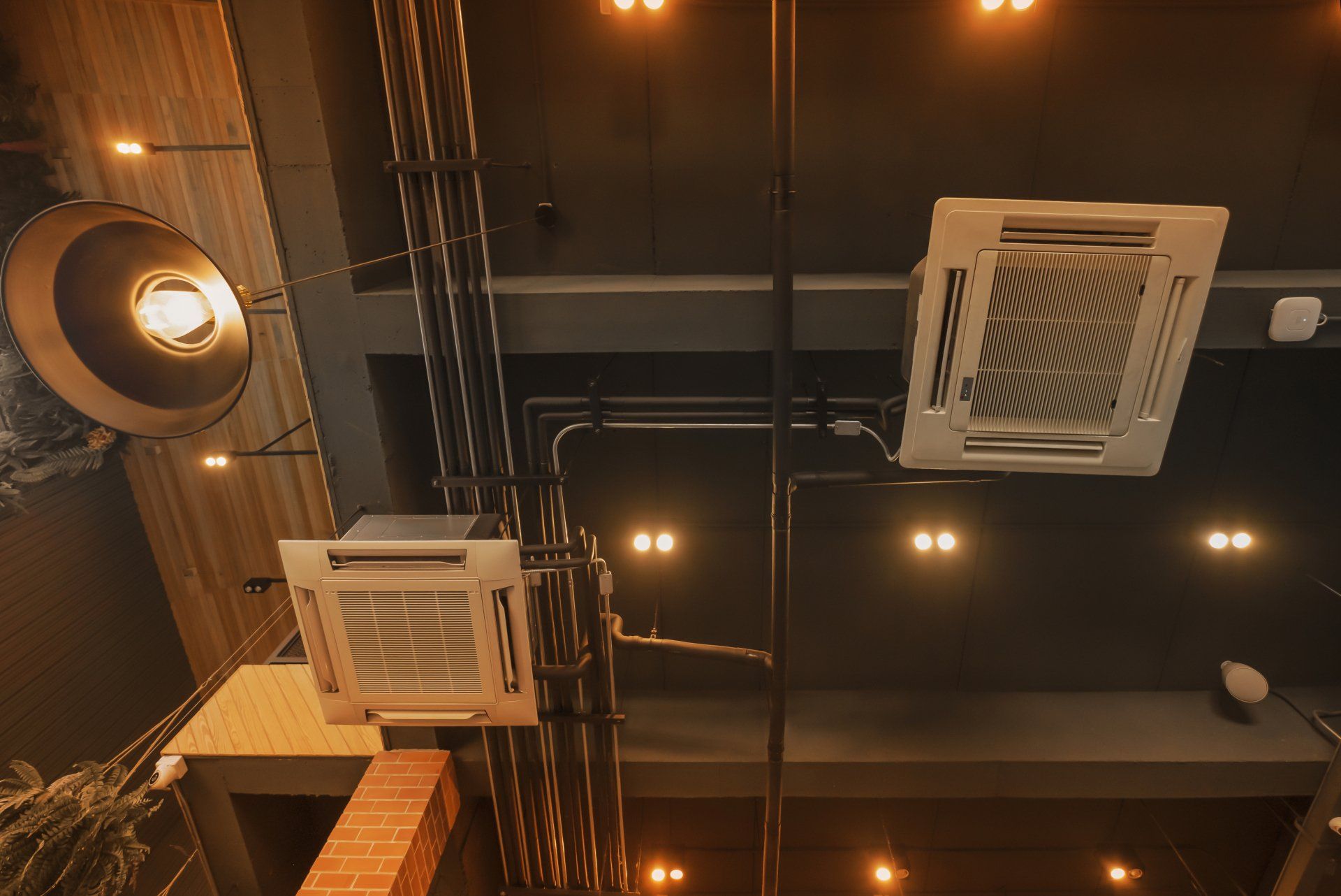 Ceiling view of industrial vents, pipes, and warm hanging lights in a dark interior