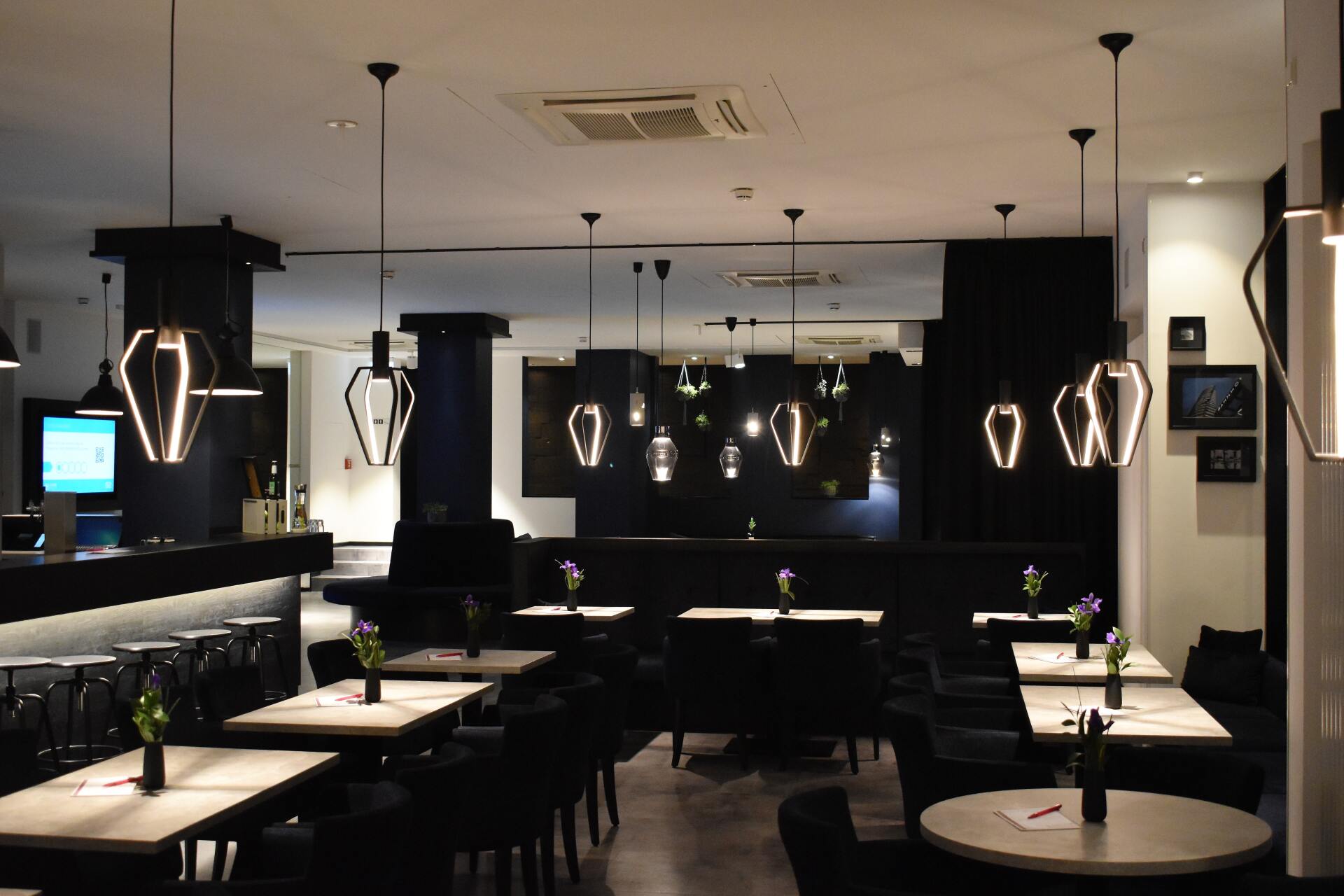 Dim modern restaurant interior with pendant lights, tables, and black decor