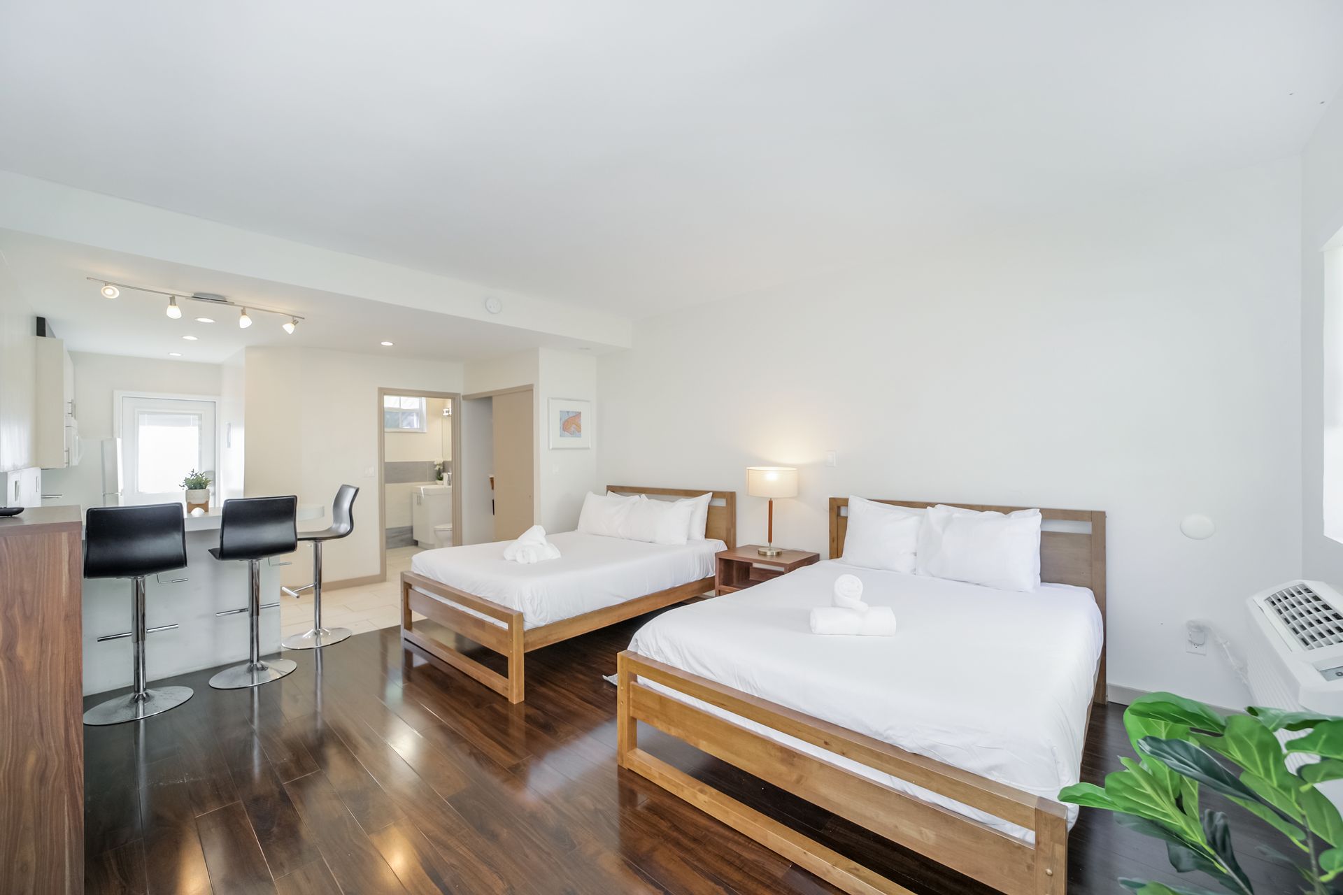 Bright modern hotel room with two queen beds, hardwood floors, and a small bar area.