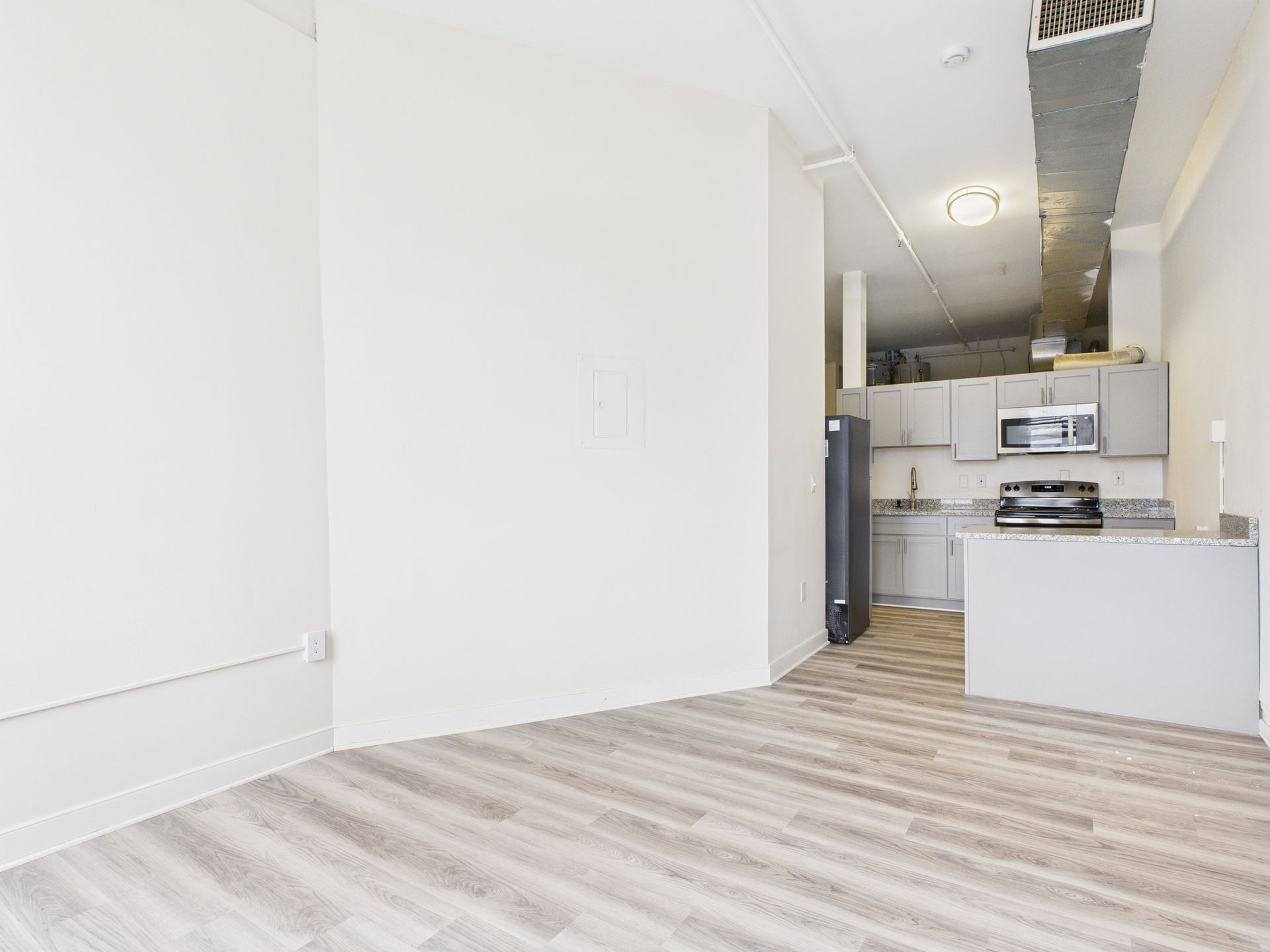 Empty modern studio apartment with gray kitchen and light wood flooring.