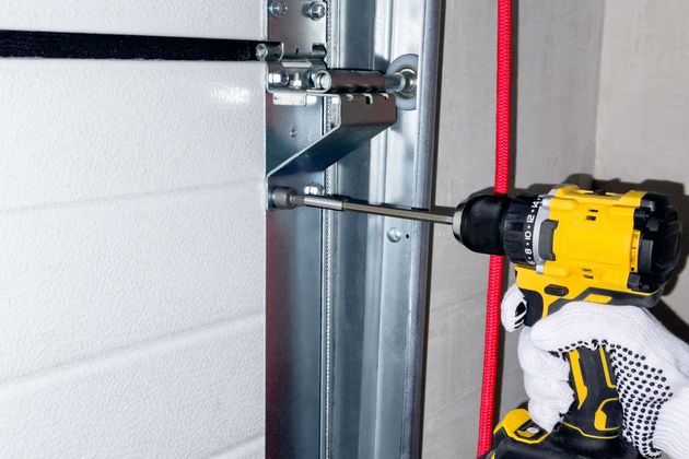 Gloved worker using a yellow drill to fasten metal framing next to insulation and a red line