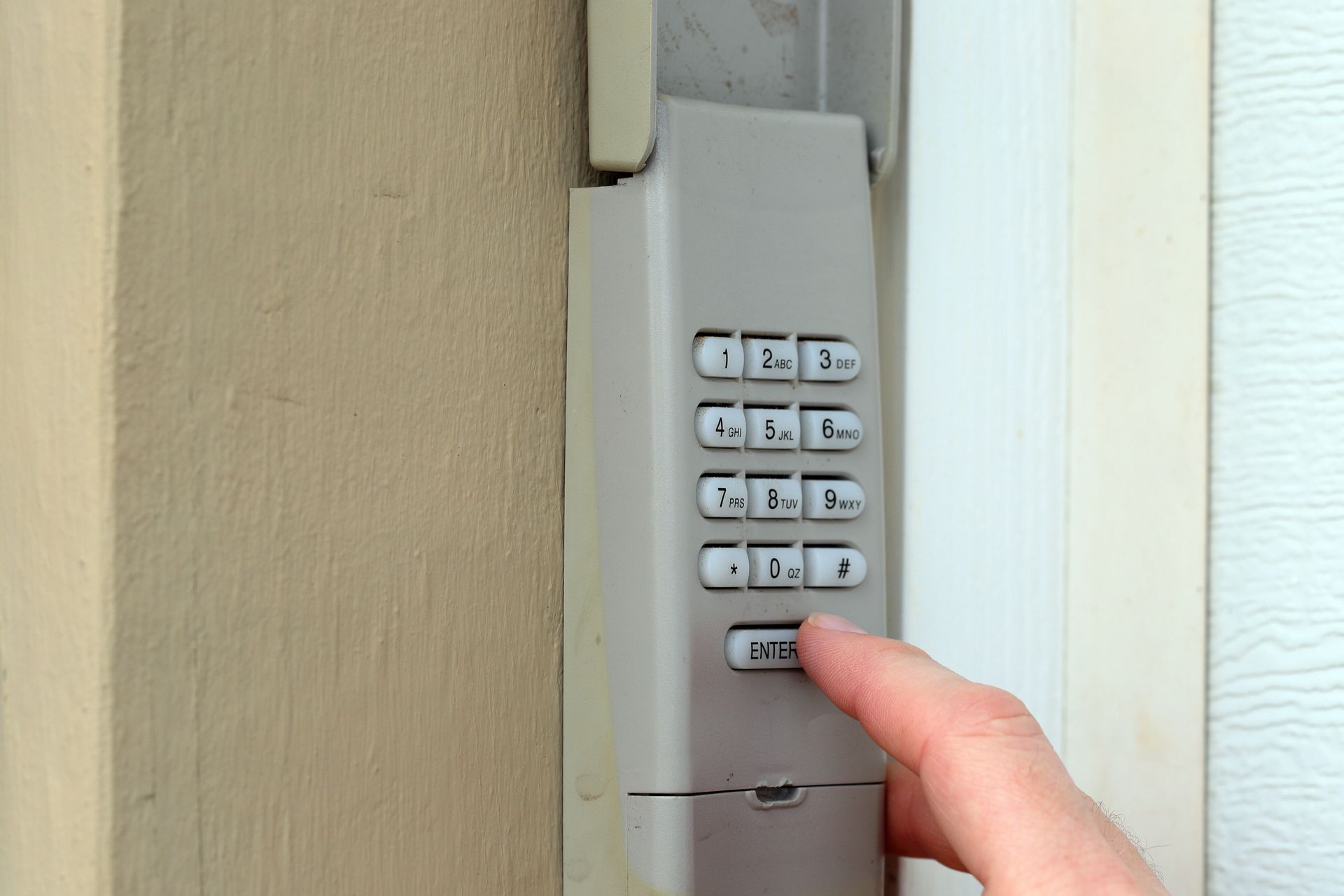 Finger pressing a keypad on a wall-mounted door lock