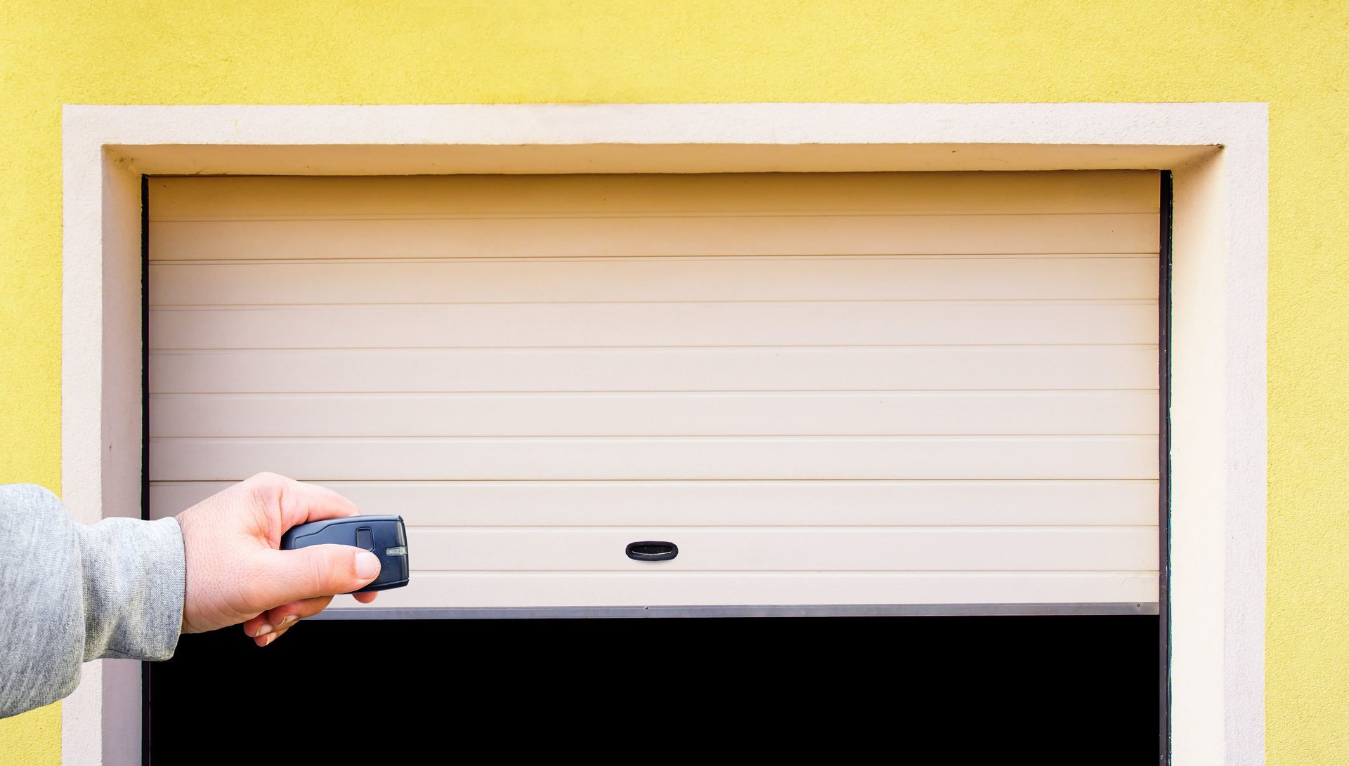 Hand opening a beige garage door with a remote opener