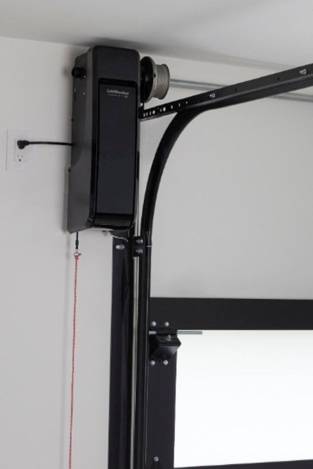 Two workers installing a garage door motor on the ceiling, with one holding the bracket and one using a tool.