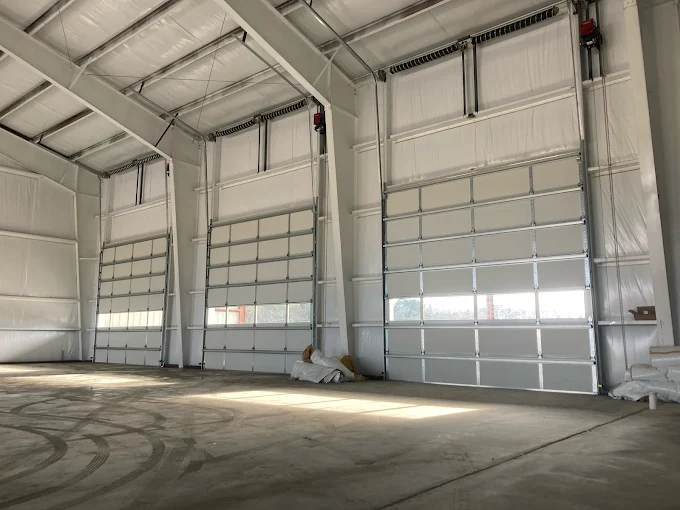 Empty industrial warehouse interior with large white roll-up doors and concrete floor