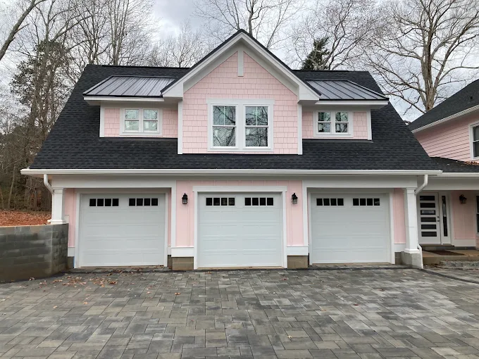 Pink-and-gray house with three white garage doors and a paved driveway