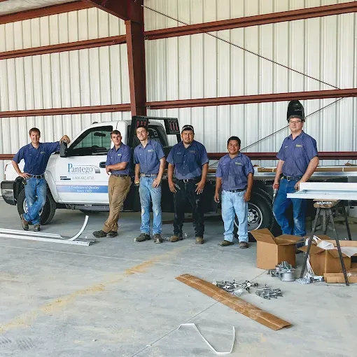 Team of workers in blue uniforms posing in a metal workshop beside a van and tools.