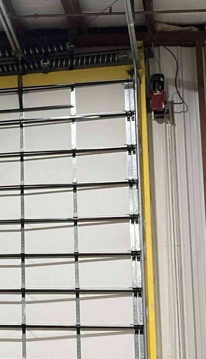 Closed white garage door with yellow trim and a red wall-mounted device near the ceiling Closed white garage door with yellow trim and a red wall-mounted device near the ceiling