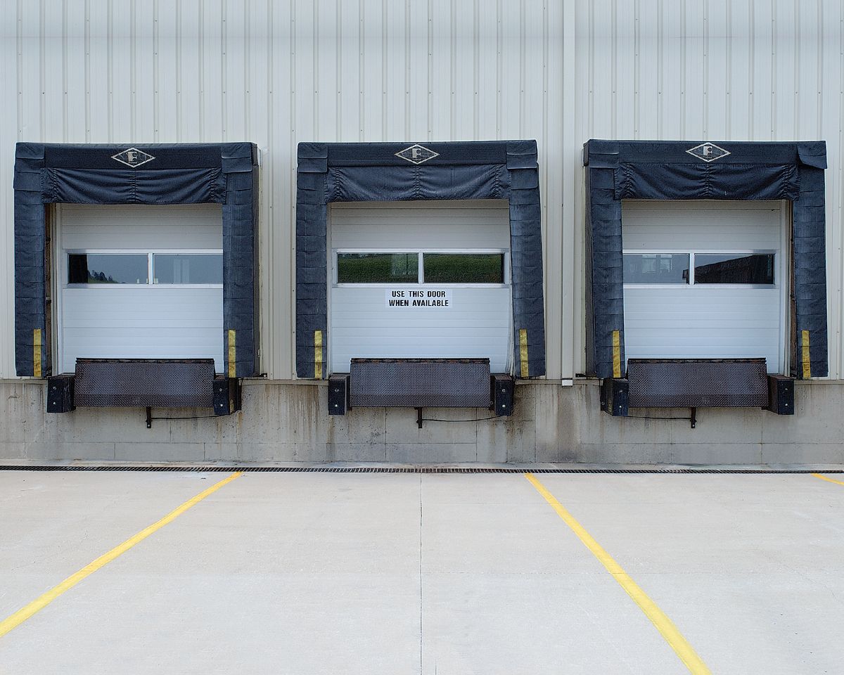 White service vans parked outside a large gray industrial building on a cloudy day